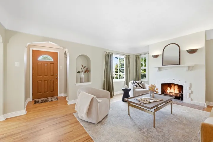 Wood-finish flooring, a paneled entry door with leaded glass, a built-in arched alcove, and a corner fireplace with a white mantel and brick surround