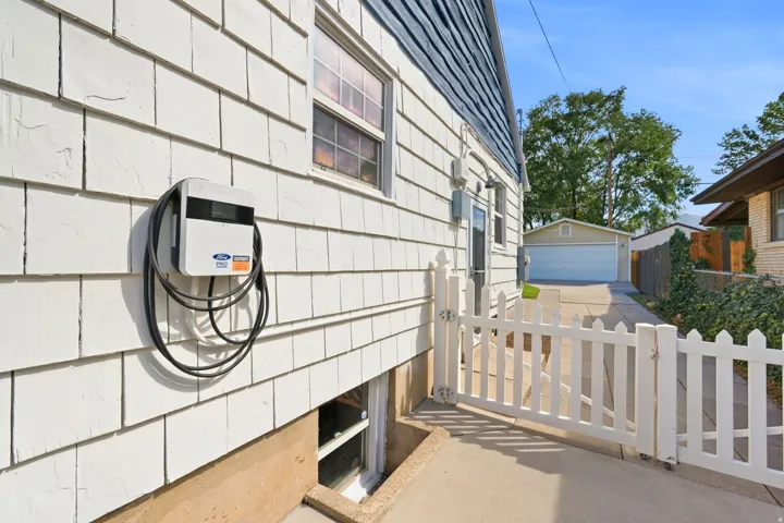 White shingle siding, basement window, electric vehicle charging station, white picket fence, concrete driveway