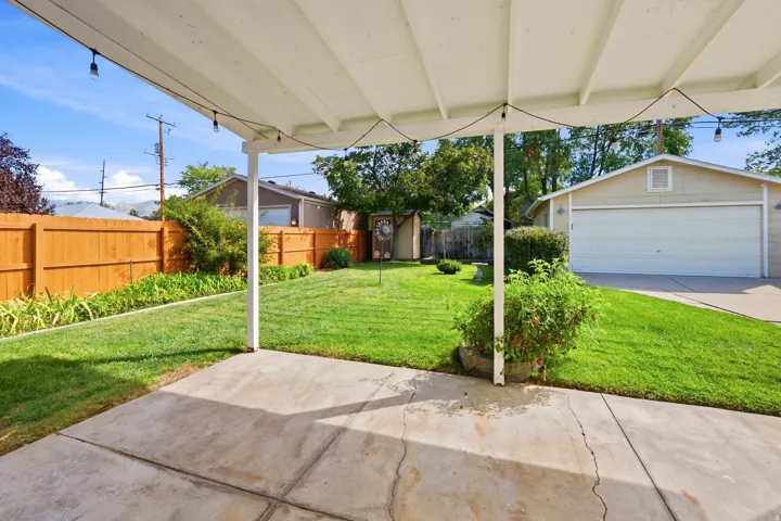 Covered patio with concrete flooring, expansive green lawn, wood privacy fence, detached garage, and garden shed