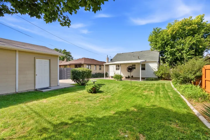 Expansive grassy yard with a detached garage, concrete driveway, and covered patio