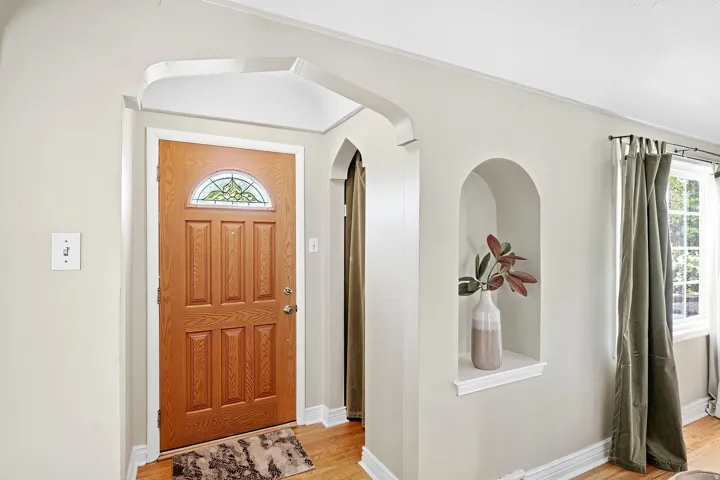 Entryway featuring a paneled wood door with stained-glass transom, arched doorways, a built-in display niche, and wood-finish flooring