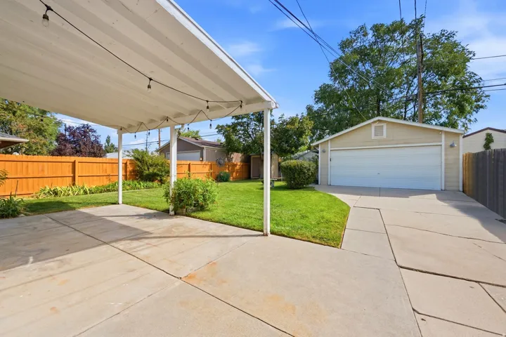 Expansive backyard featuring a covered patio, concrete paving, a manicured lawn, wood fencing, and a detached two-car garage