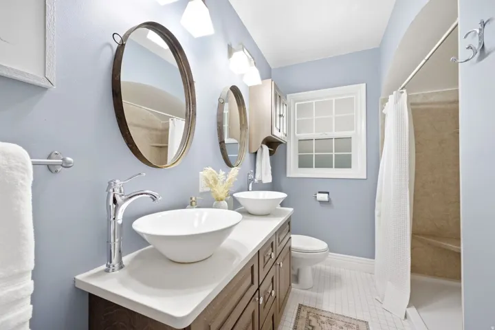 Dual vessel sinks set atop a wood-finish vanity with a light-toned countertop