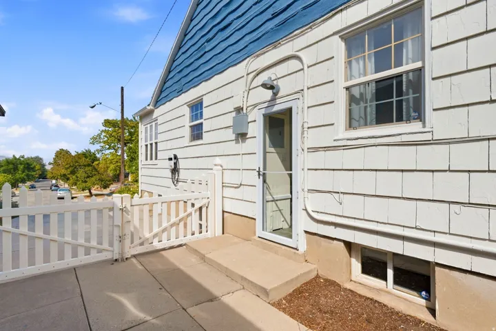 White picket fencing, concrete patio, blue shingle siding, white shingle siding, and a security screen door