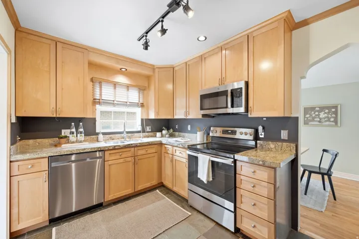 Kitchen featuring stainless steel appliances, light wood-finish cabinetry, stone-finish countertops, track lighting, and under-cabinet lighting