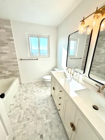 Dual vanity with integrated sinks, modern gold-tone hardware, and a coordinating light fixture
