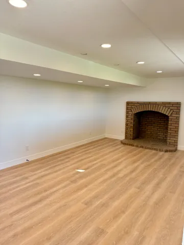 Wood-finish flooring, recessed lighting, white walls, and a brick fireplace with a hearth