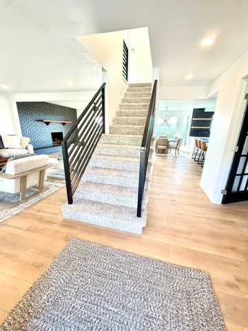 Wood-finish flooring throughout, carpeted staircase with contemporary metal railings, and recessed ceiling lighting