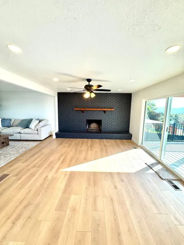 Spacious living area featuring wood-finish flooring, a black brick fireplace with a wood mantel, and recessed lighting