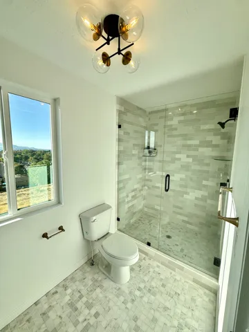 Spacious walk-in shower with glass enclosure and subway tile surround, white tile flooring, and a modern ceiling-mounted light fixture
