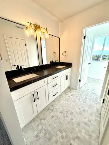 Dual vanity with white cabinetry, black hardware, dark countertops, and undermount sinks