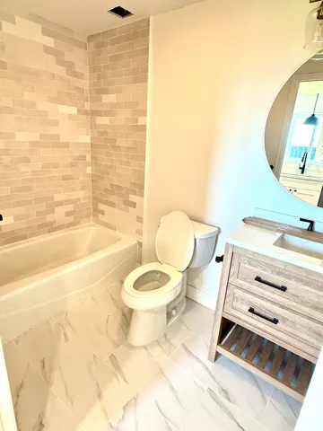 Bathtub with subway tile surround, sleek white toilet, and wood-finish vanity with built-in shelving