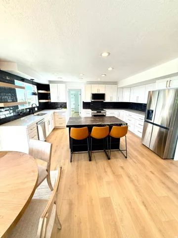 Light wood-finish flooring throughout, white cabinetry, dark subway tile backsplash, recessed lighting, and stainless steel appliances