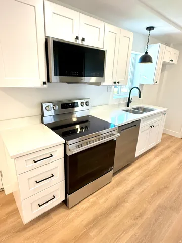 White shaker cabinetry, stainless steel appliances, light-toned wood-finish flooring, undermount dual-basin sink, and a black gooseneck faucet