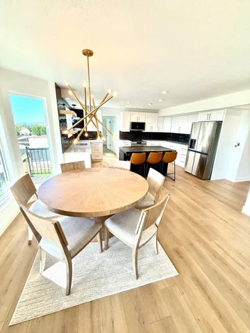 Open-concept space featuring wood-finish flooring, a contemporary chandelier, white cabinetry, dark tile backsplash, and stainless steel appliances