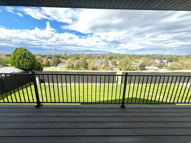 Expansive outdoor deck with composite decking and black metal railing overlooking a landscaped backyard and distant scenery