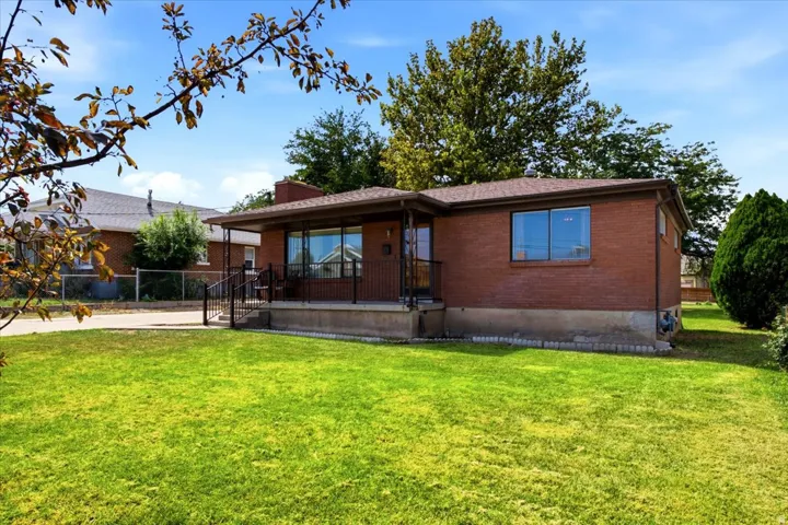 Brick exterior with a covered porch featuring metal railings, a front lawn, and mature trees