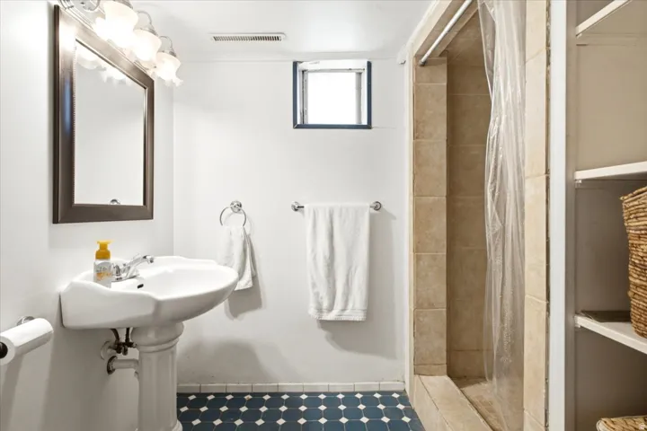 Pedestal sink, framed mirror, vanity lighting, tiled shower, and built-in shelving