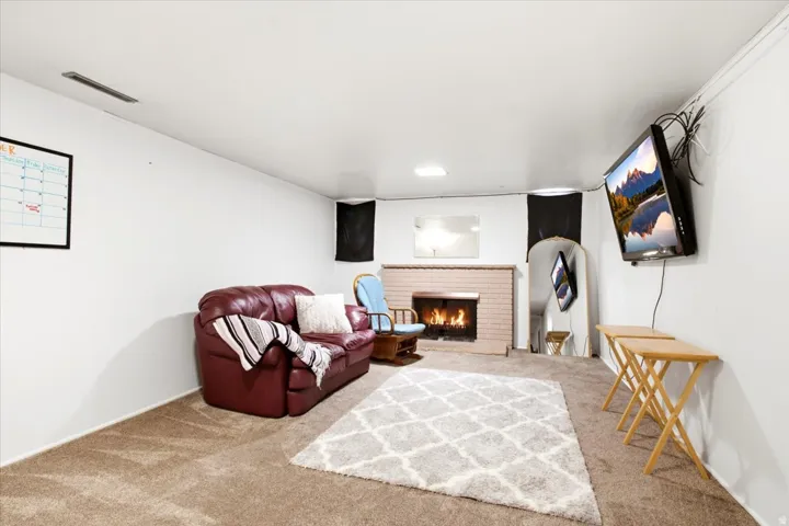 Carpeted living space featuring a brick fireplace with a mantel, a wall-mounted television, and recessed ceiling lighting