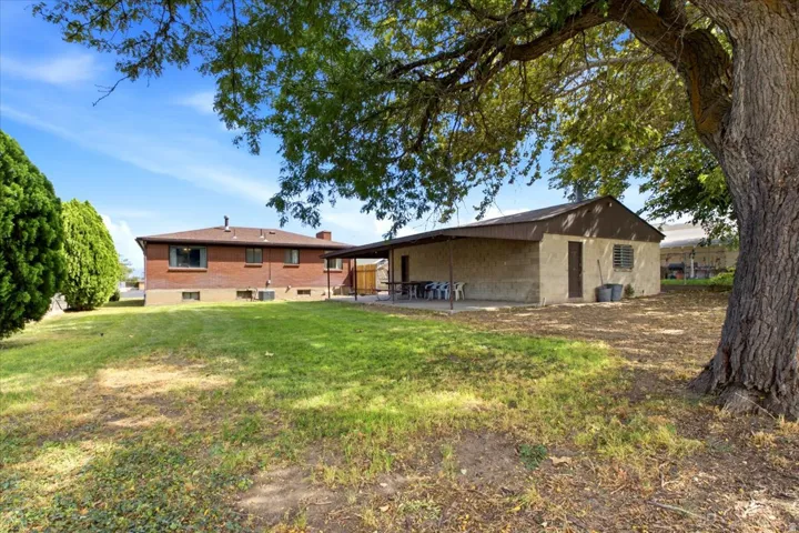 Expansive outdoor space featuring a red brick exterior, a substantial shade tree, and an additional detached structure with a covered patio