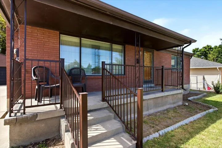Brick exterior with a covered porch featuring decorative metal railings and concrete steps