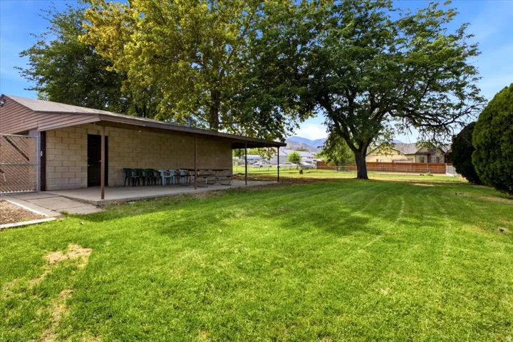 Expansive green space with mature trees and a solid block structure featuring a covered concrete patio