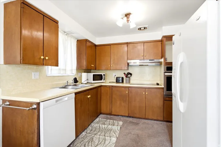 Kitchen featuring wood-finish cabinetry, light-toned countertops, a double basin sink, and a built-in oven