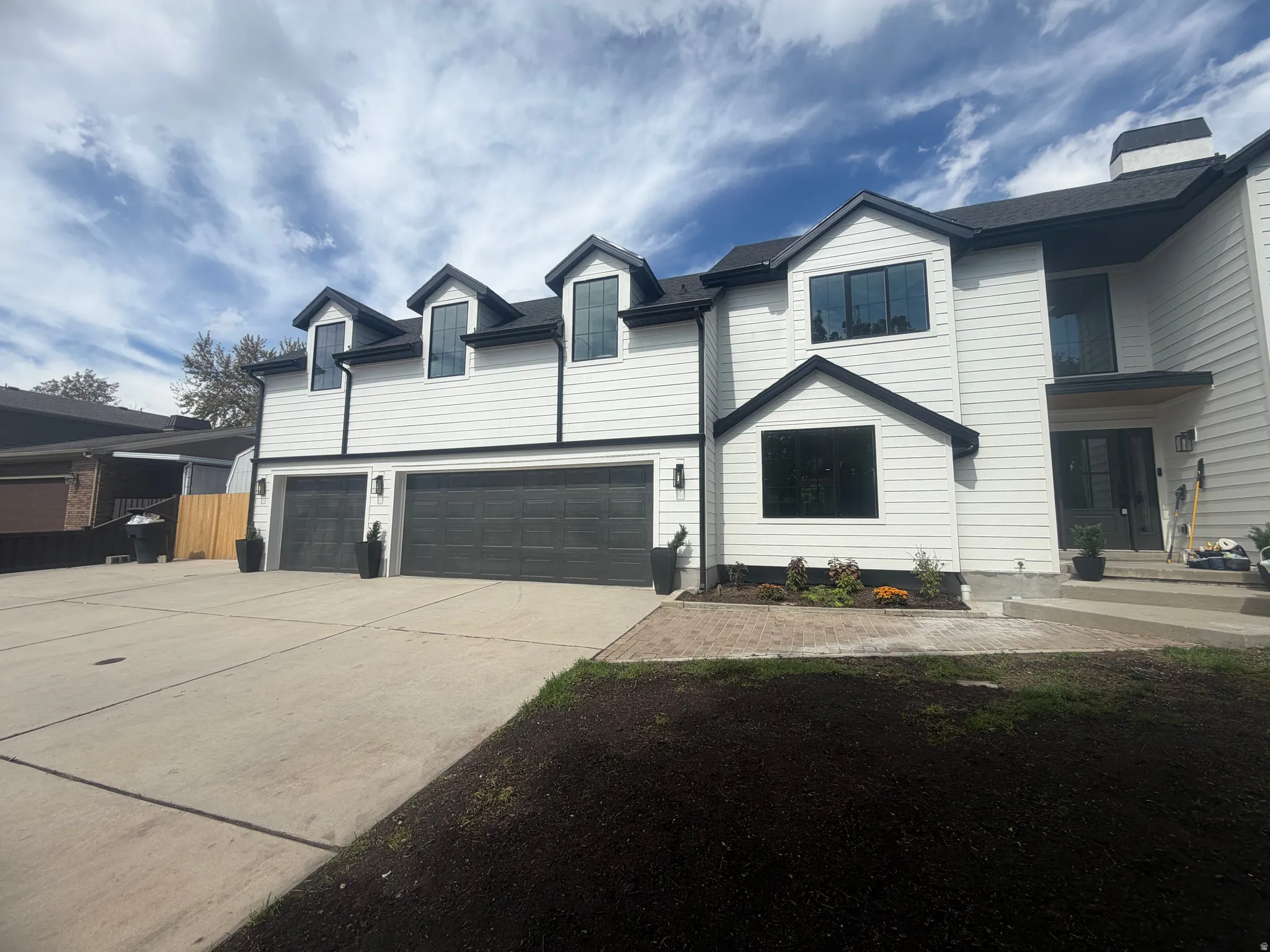 White horizontal siding with dark trim, dual garage doors, dormer windows, and a concrete driveway