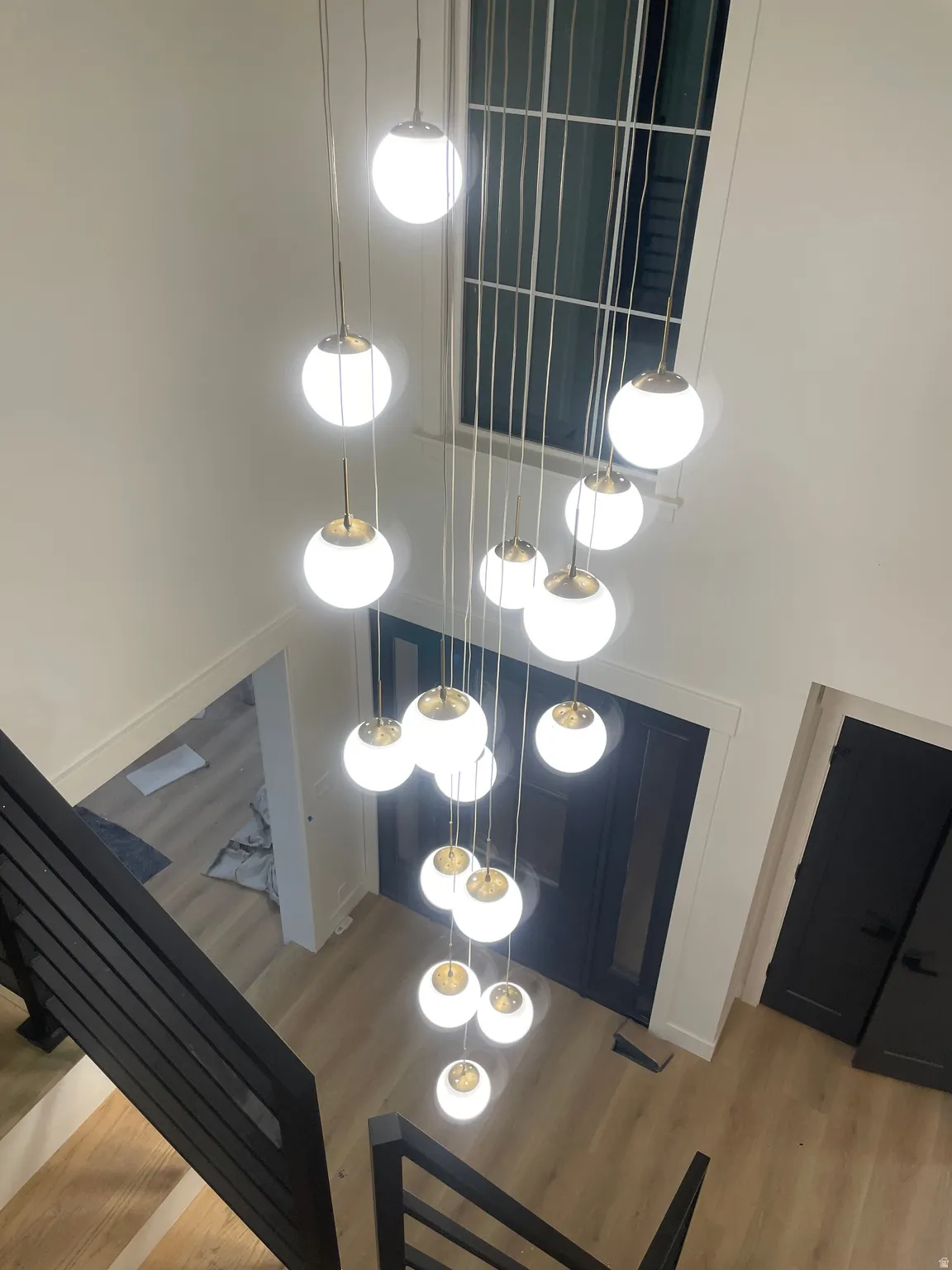 Multi-story chandelier with spherical lights, large transom window, light wood-finish flooring, and black interior doors