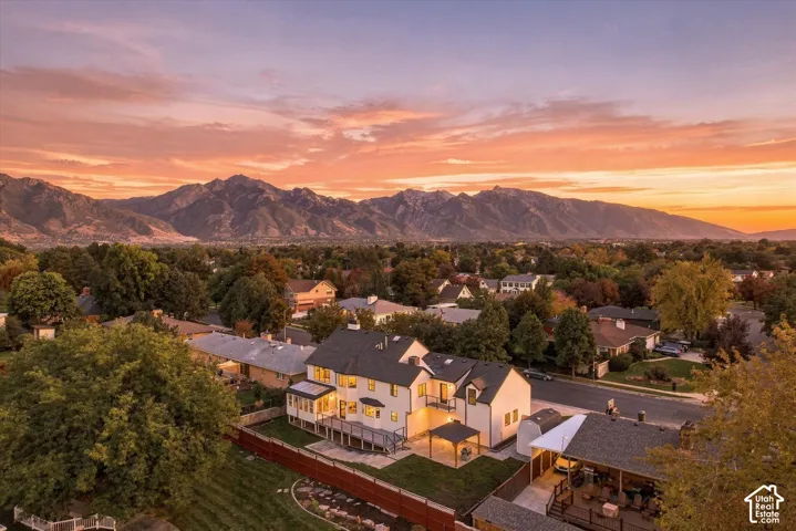 Expansive mountain backdrop, established neighborhood with mature trees, multi-level dwelling with dark roofing, rear deck, and covered patio