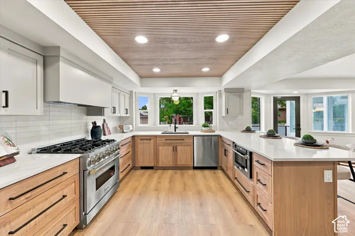 Gourmet kitchen featuring a wood-slat ceiling, light wood-finish flooring, white quartz countertops, full tile backsplash, and stainless steel appliances