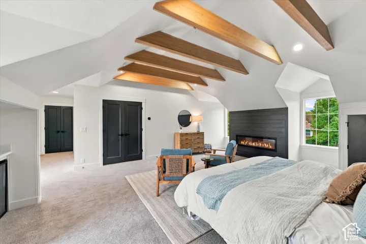 Vaulted ceiling with exposed wood beams, built-in linear fireplace with shiplap surround, and dark paneled doors