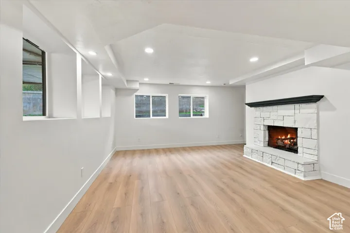 Hardwood-finish flooring, recessed lighting, white stone-clad fireplace with black mantle, multiple windows, and a neutral color palette