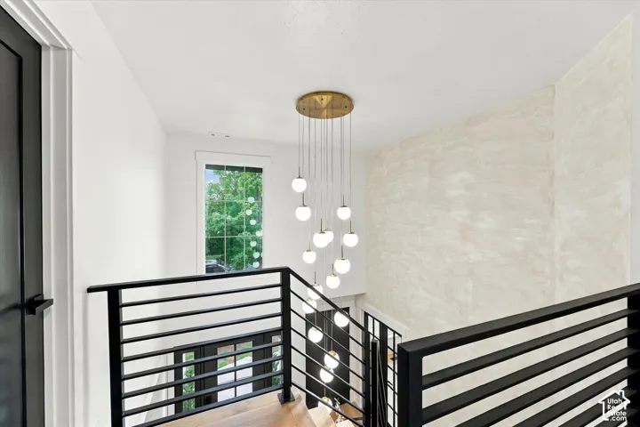 Modern chandelier, horizontal metal railing, wood-finish flooring, accent wall with textured finish, and window with exterior greenery