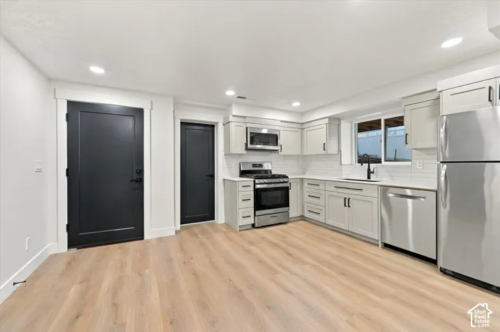 Full kitchen featuring stainless steel appliances, light wood-finish flooring, white subway tile backsplash, light grey cabinetry with dark hardware, and recessed lighting