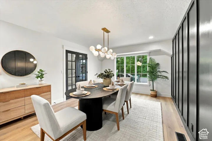 Light wood-finish flooring, a contemporary chandelier, large picture window, and black frame French doors