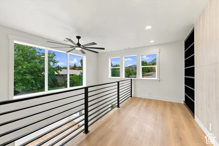 Open loft space with wood-finish flooring, contemporary black metal railing, a ceiling fan, and recessed lighting