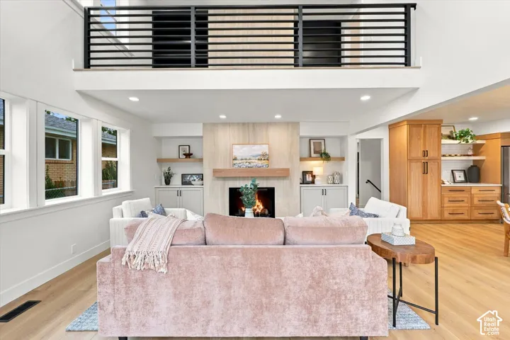 Open-concept living space featuring a fireplace with a wood mantel, wood-finish flooring, a vaulted ceiling, and an interior balcony with a black railing