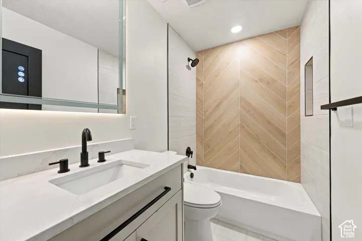 Vanity with a white countertop and integrated sink, matte black fixtures, an illuminated mirror, and a bathtub with a herringbone-patterned tile surround