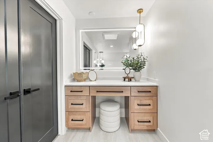Built-in vanity with wood-finish cabinetry, a light-toned countertop, and an integrated illuminated mirror