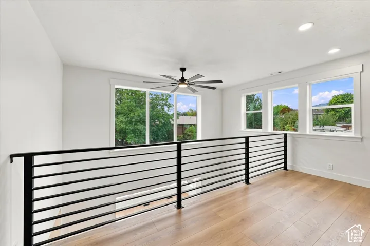 Open loft area with wood-finish flooring, a contemporary black metal railing, multiple windows, and recessed lighting
