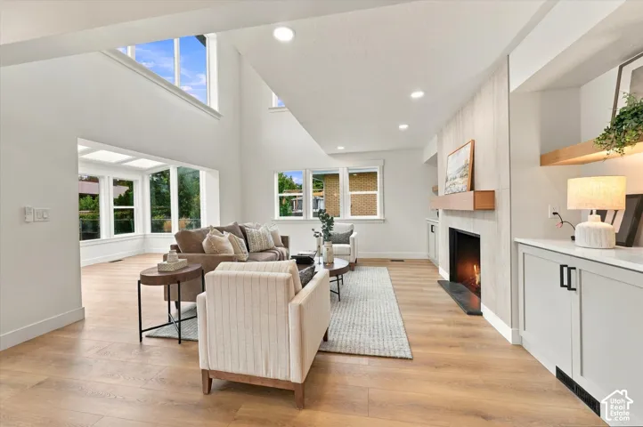 Open-concept living area with soaring ceilings, wood-finish flooring, a fireplace with a wood mantle, recessed lighting, and built-in cabinetry with a countertop