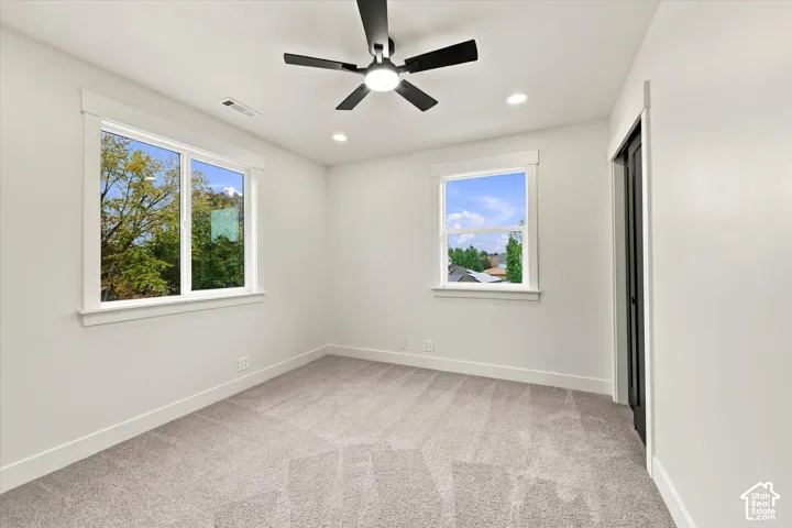 Neutral-toned carpeting, two white-trimmed windows, a black ceiling fan, and recessed lighting