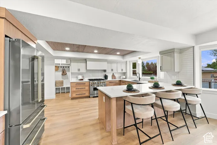 Open-concept kitchen featuring an island with counter seating, stainless steel appliances, light-toned wood-finish flooring, and a recessed ceiling with wood paneling