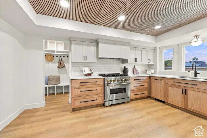 Contemporary kitchen with wood-finish flooring, two-tone cabinetry, stainless steel range, white subway tile backsplash, and a built-in mudroom bench
