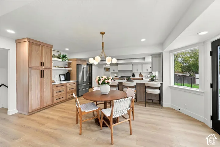 Expansive wood-finish flooring, custom wood cabinetry, stainless steel refrigerator, white subway tile backsplash, and a large bay window