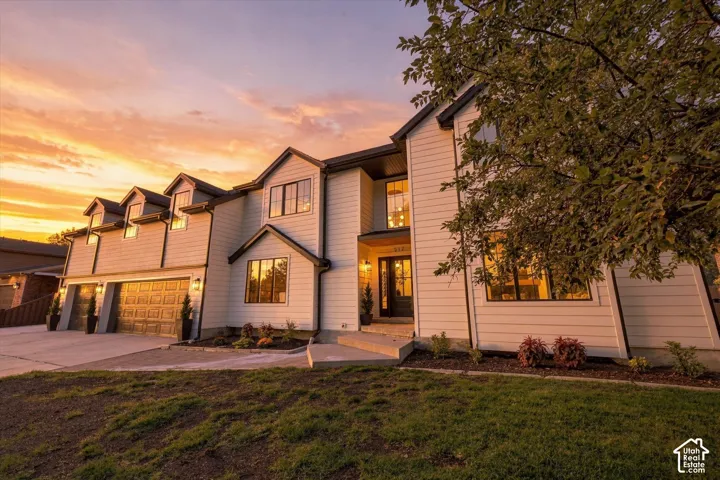 Contemporary-style residence featuring white horizontal siding, black-framed windows, a double garage with decorative doors, and multiple gabled dormers