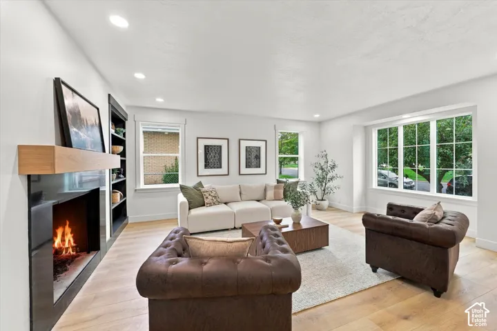 Recessed lighting, wood-finish flooring, built-in shelving, large windows with grilles, and a fireplace with a wood mantle