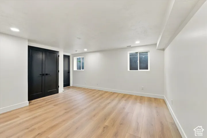 Spacious room featuring wood-finish flooring, white walls, recessed lighting, and black double doors