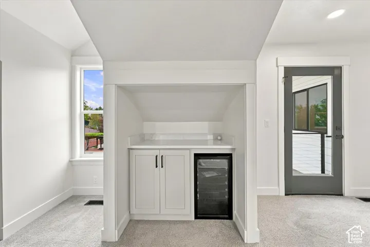 Built-in wet bar with white cabinetry, solid surface countertop, beverage refrigerator, and recessed lighting